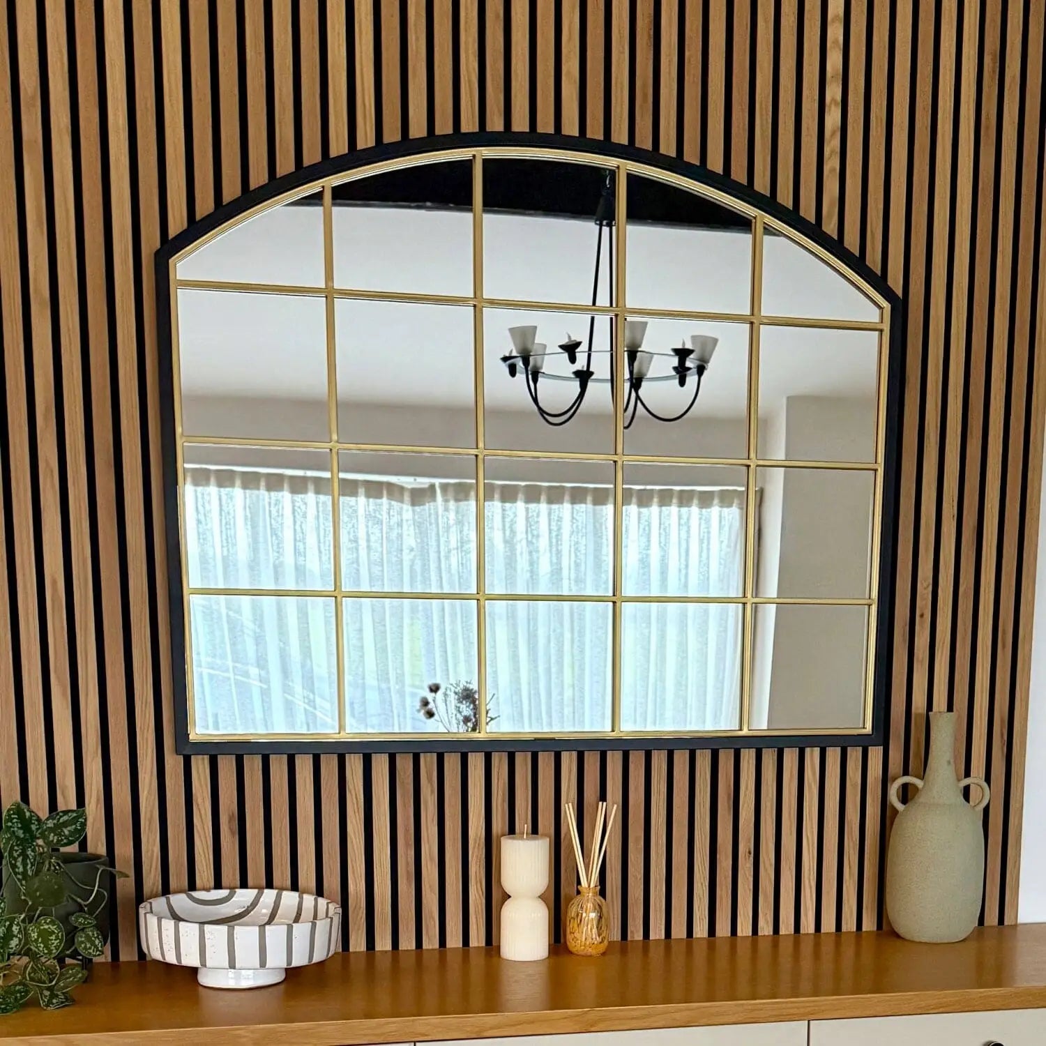 Arched window-style mirror with a black frame and gold-toned grid lines.