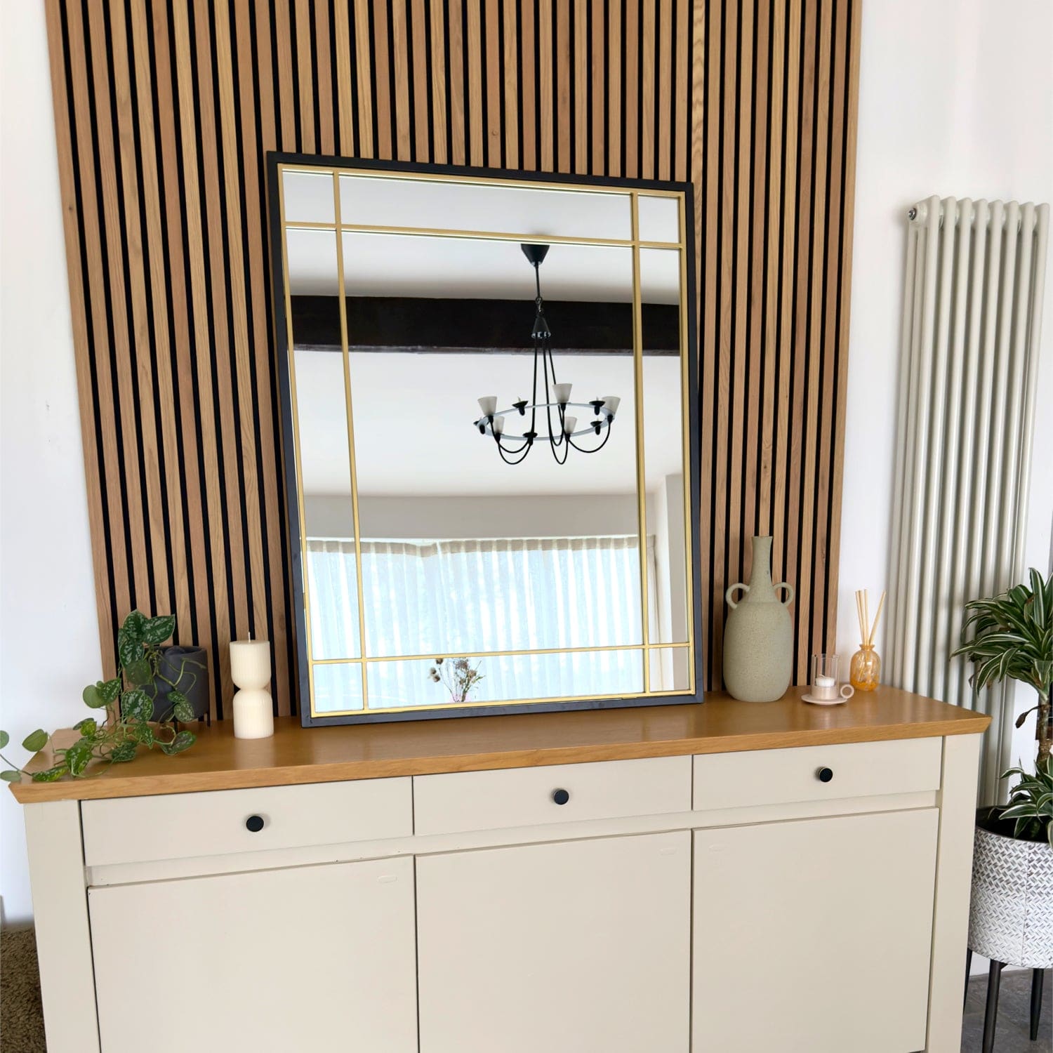 White credenza with wooden top and black knobs beneath a gold-framed mirror.