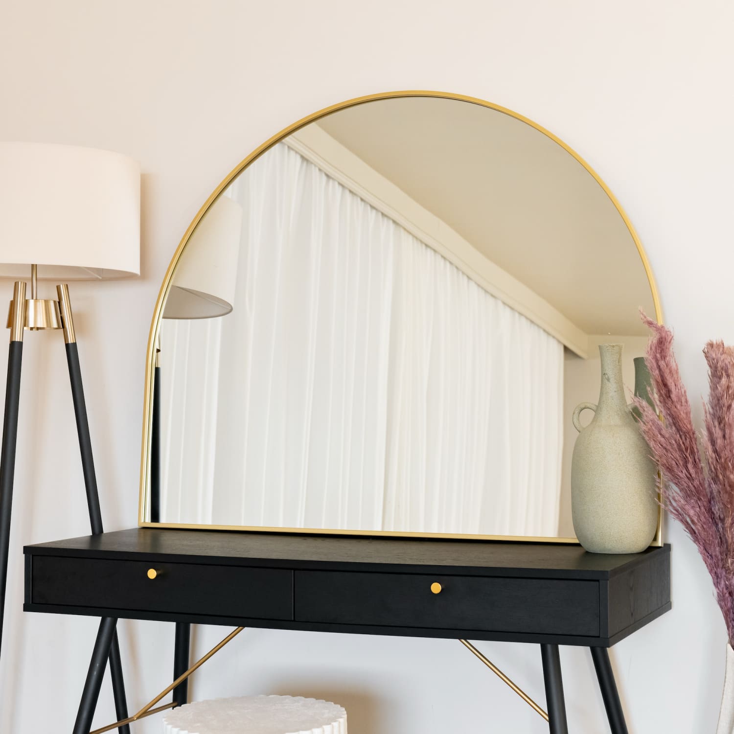 Modern vanity table with a gold-rimmed arched mirror and black drawers.