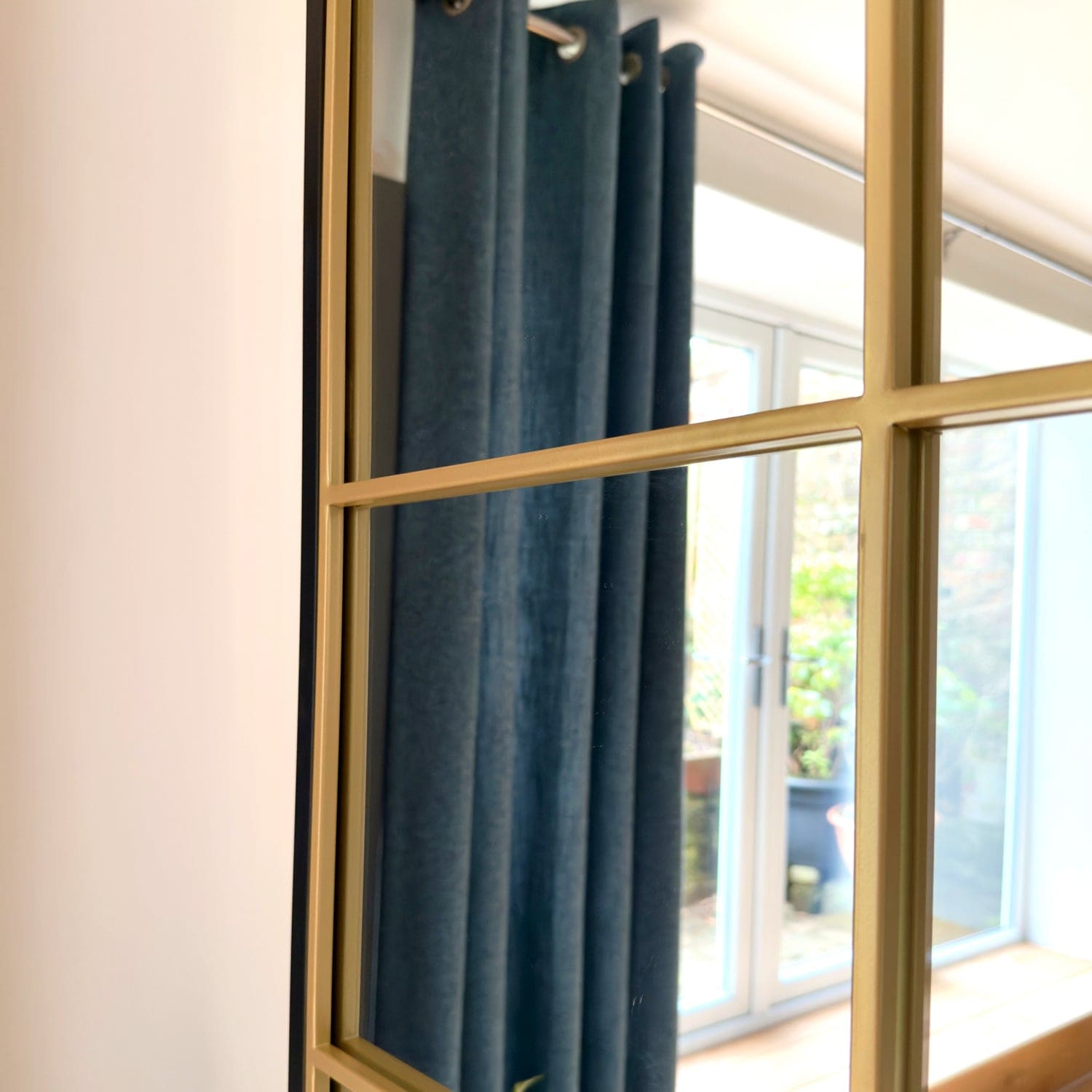 Gold-framed mirror reflecting blue curtains and a patio.