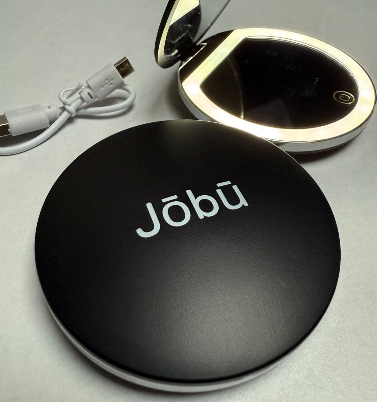 Black circular jobu travel mirror with built-in led light and usb charging cable.