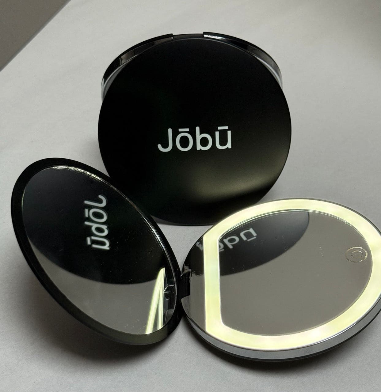 Black compact mirror with jobu branding and illuminated edge.