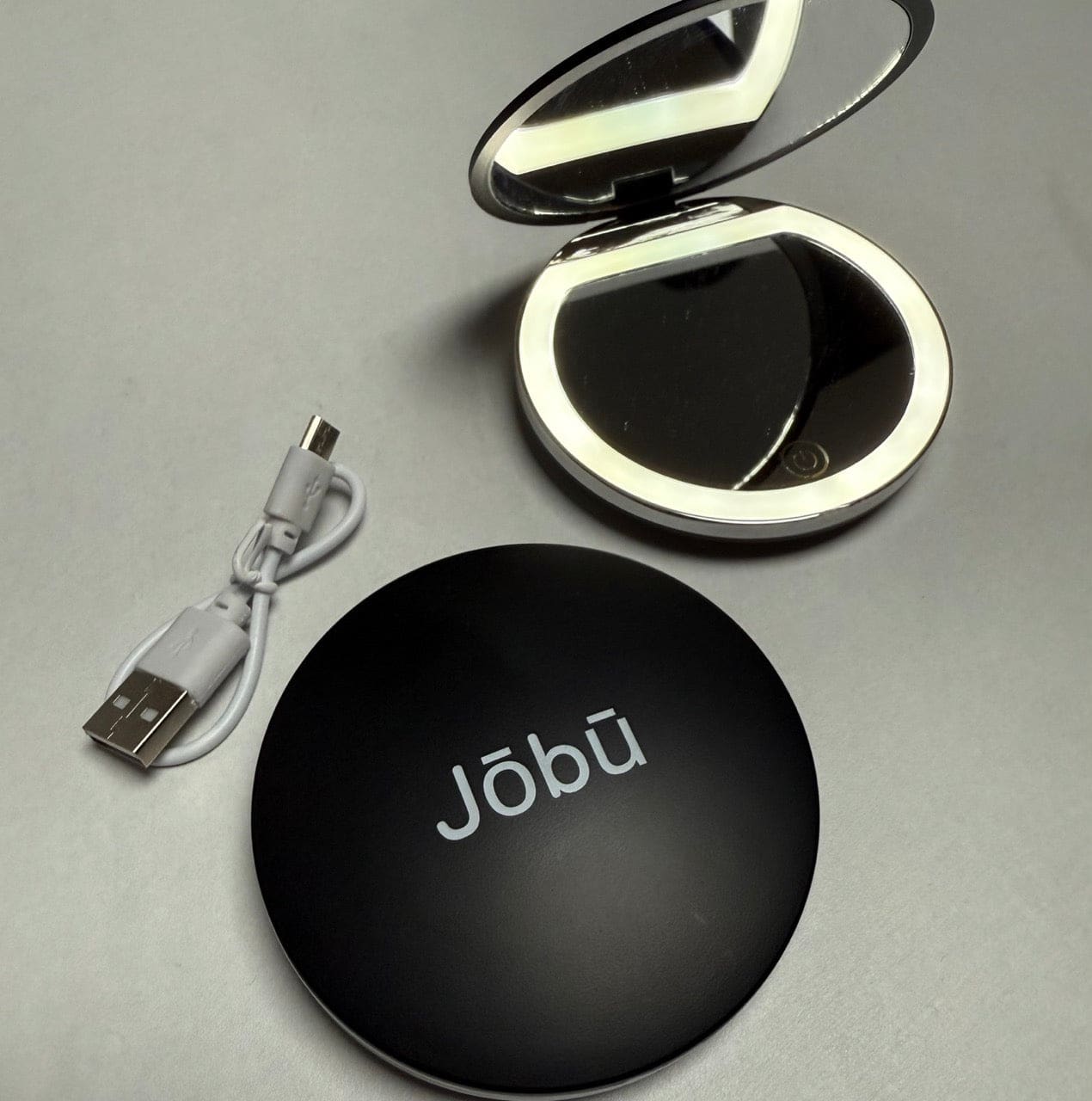 Black compact mirror with jobu branding and usb charging cable.