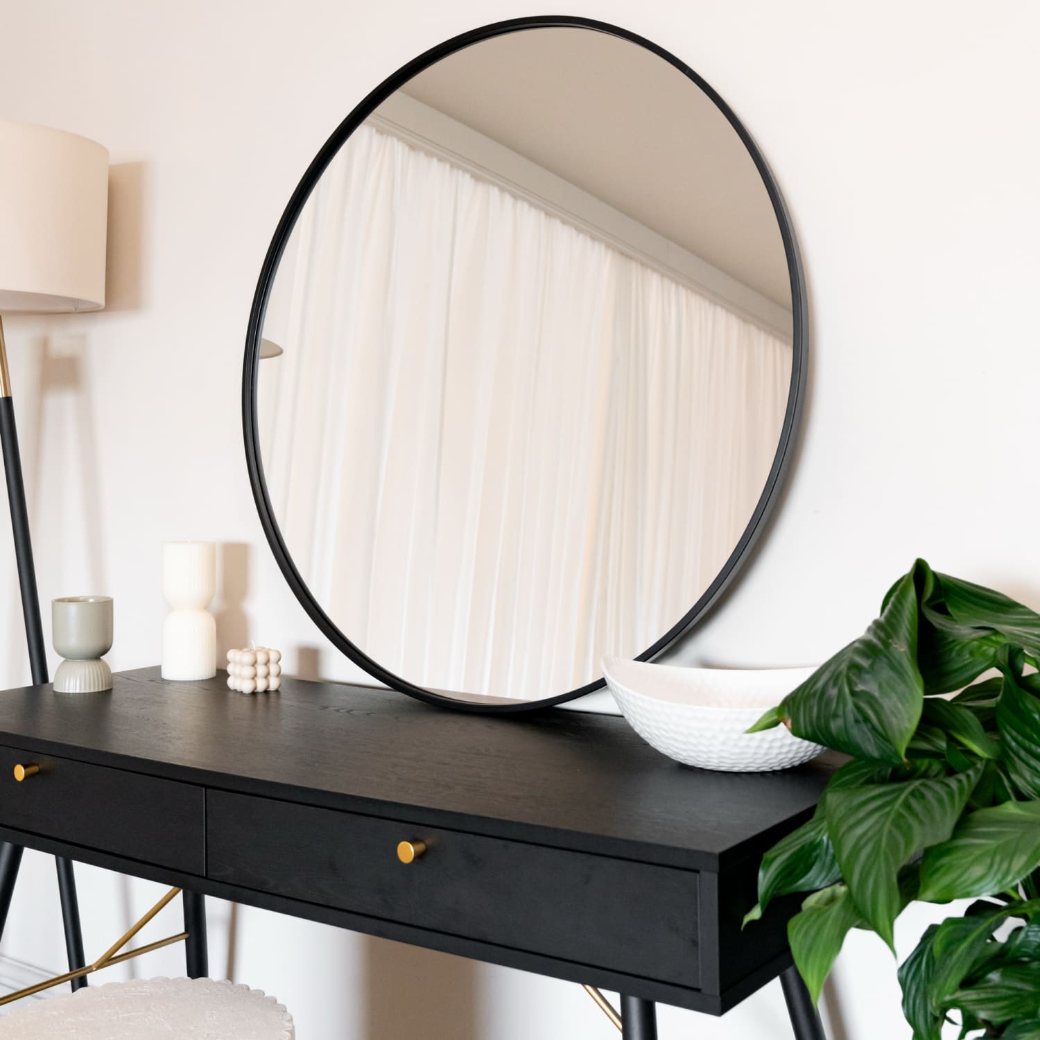 Round black-framed mirror mounted above a dark console table.