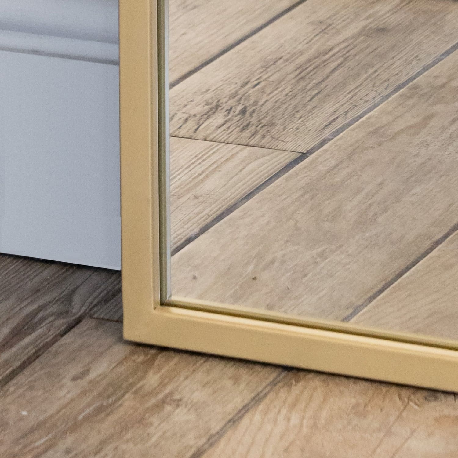 Bottom corner of a gold-framed mirror reflecting a wooden floor.