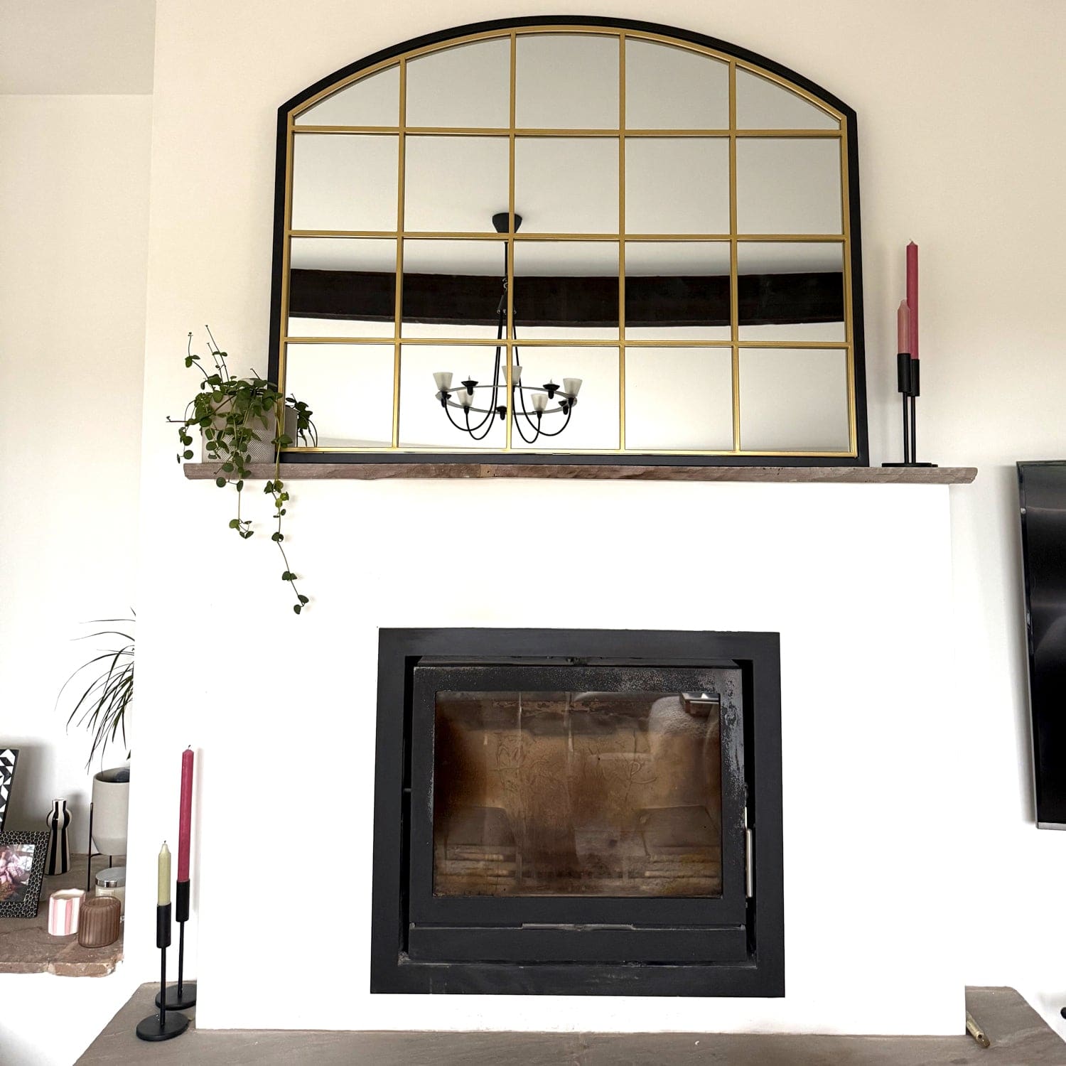 Black-framed fireplace insert with a decorative arched mirror mounted above it.