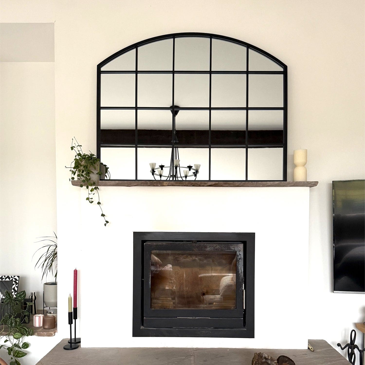 Arched window-style mirror mounted above a black fireplace insert.