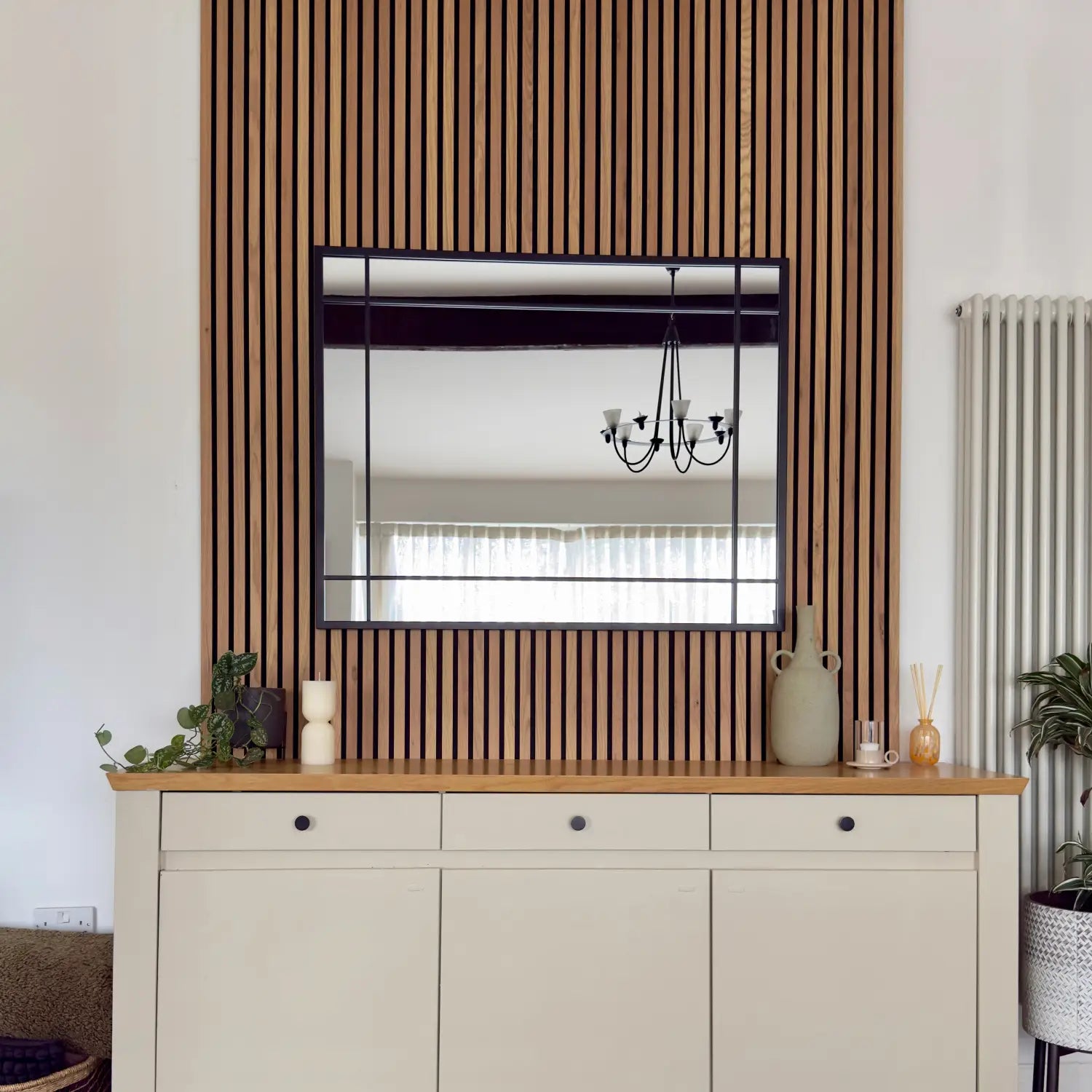 Mirror mounted on a wood-slatted accent wall above a cream-colored cabinet.