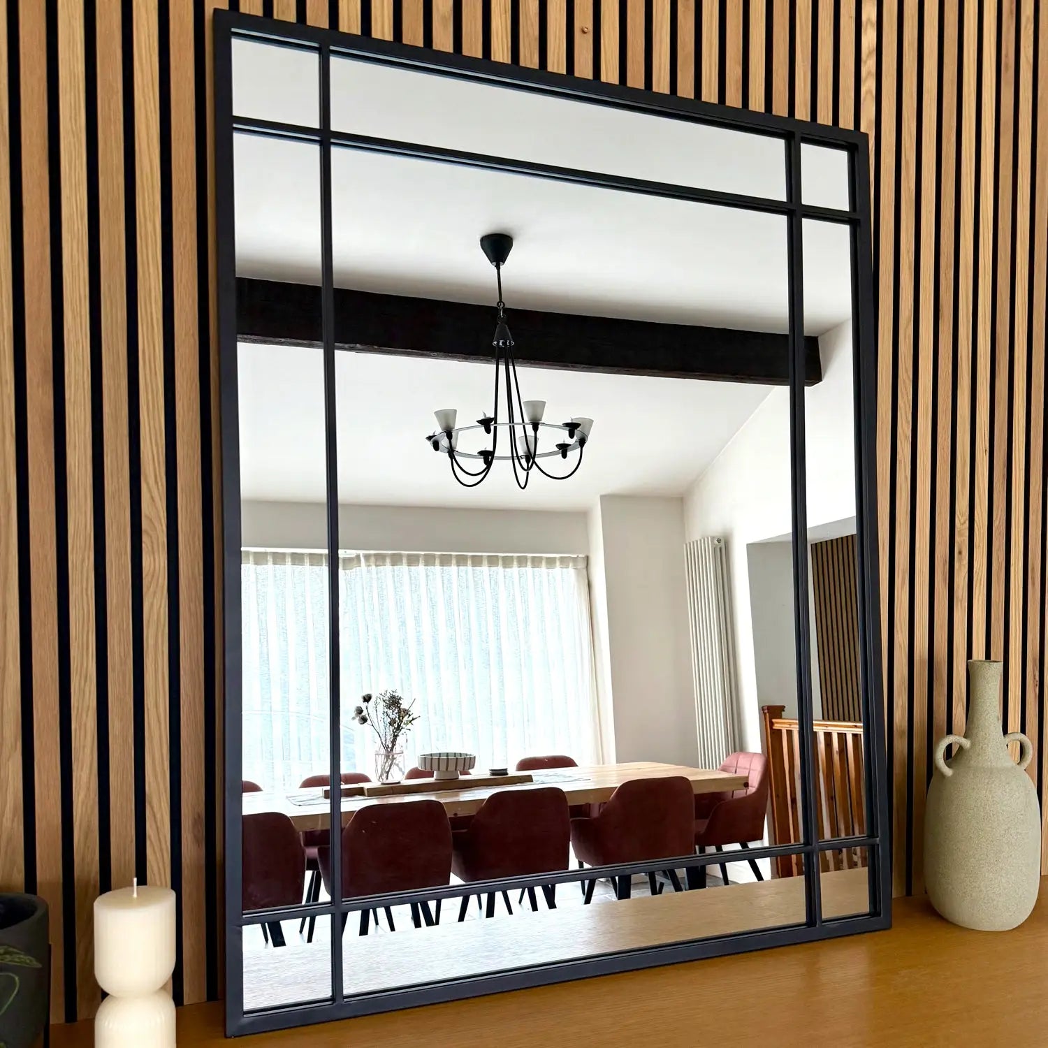 Square black-framed mirror reflecting a dining room chandelier.