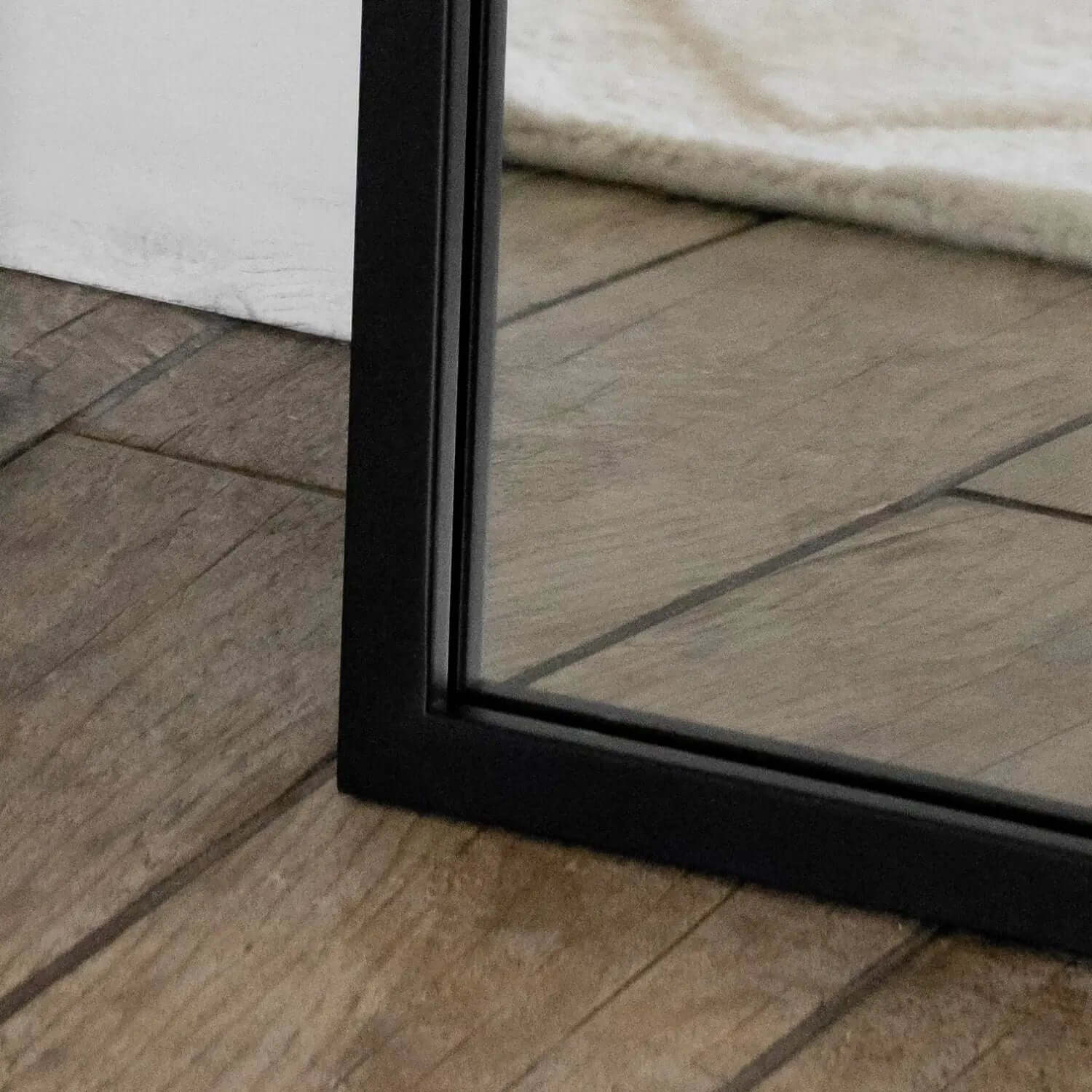 Black-framed mirror resting on wooden flooring.