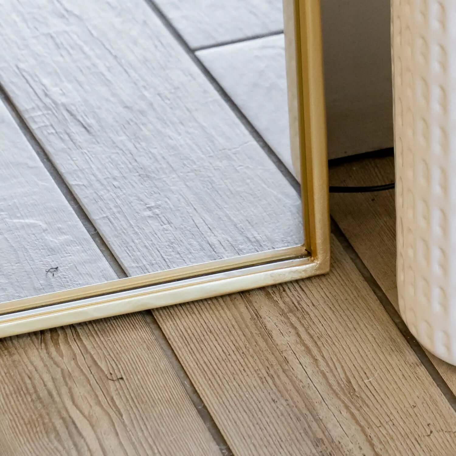 Gold-framed mirror edge resting on wooden floorboards.