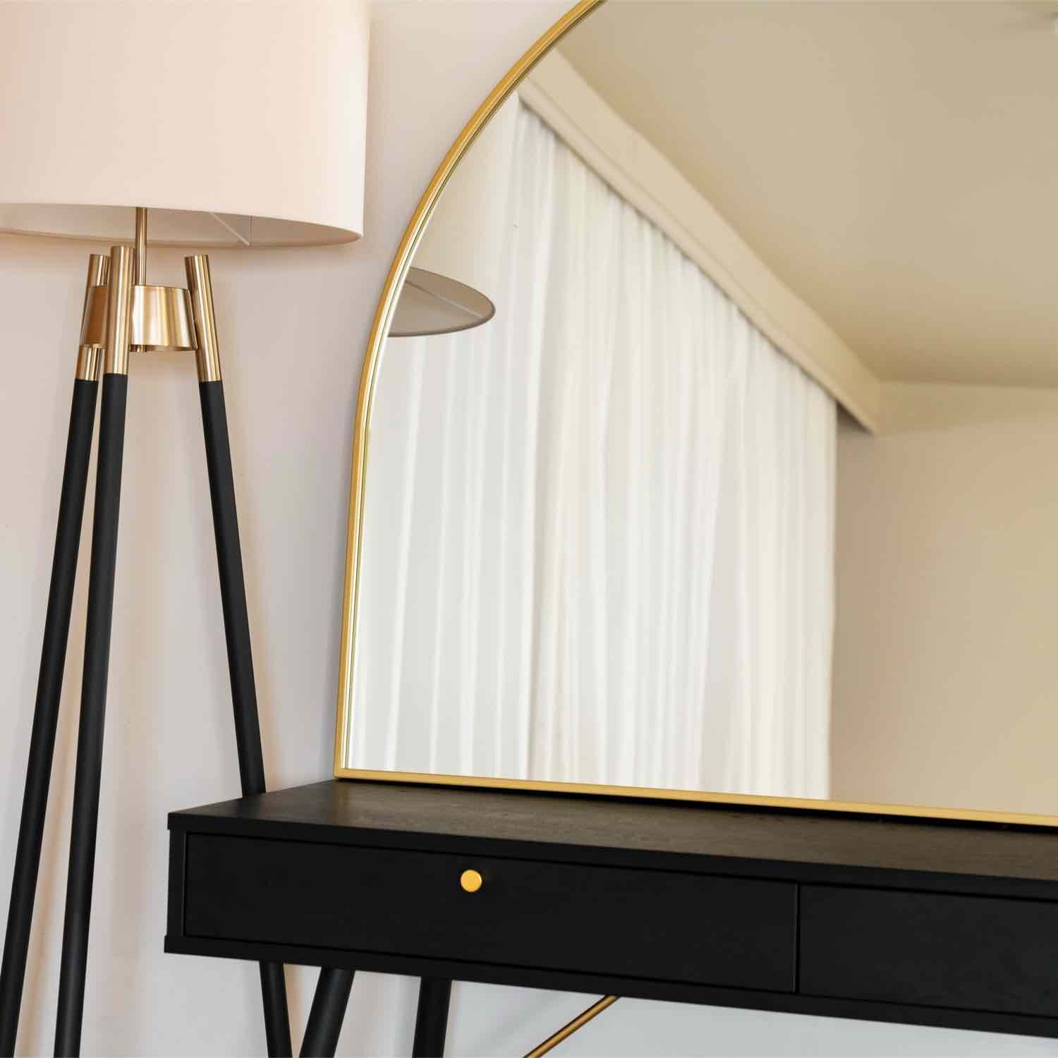 Round mirror with a thin gold frame mounted above a black desk.