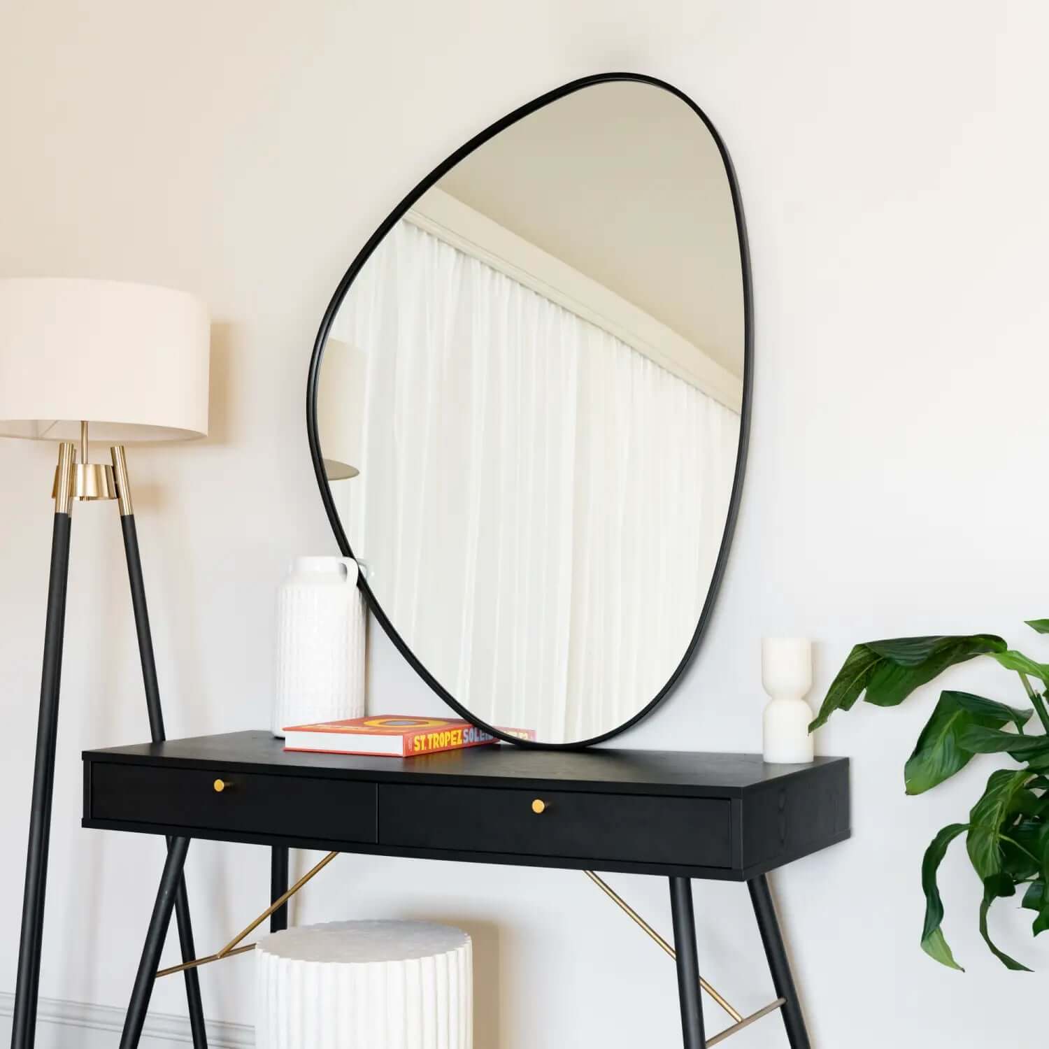 Irregularly-shaped mirror with black metal frame mounted above a black console table.