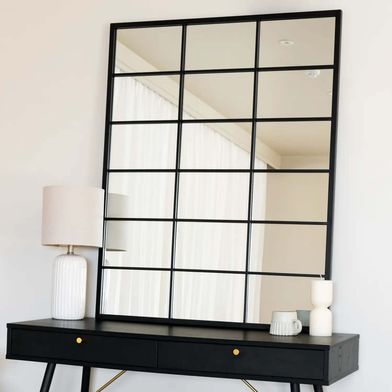 Grid-style mirror with black metal frame mounted above a black console table.