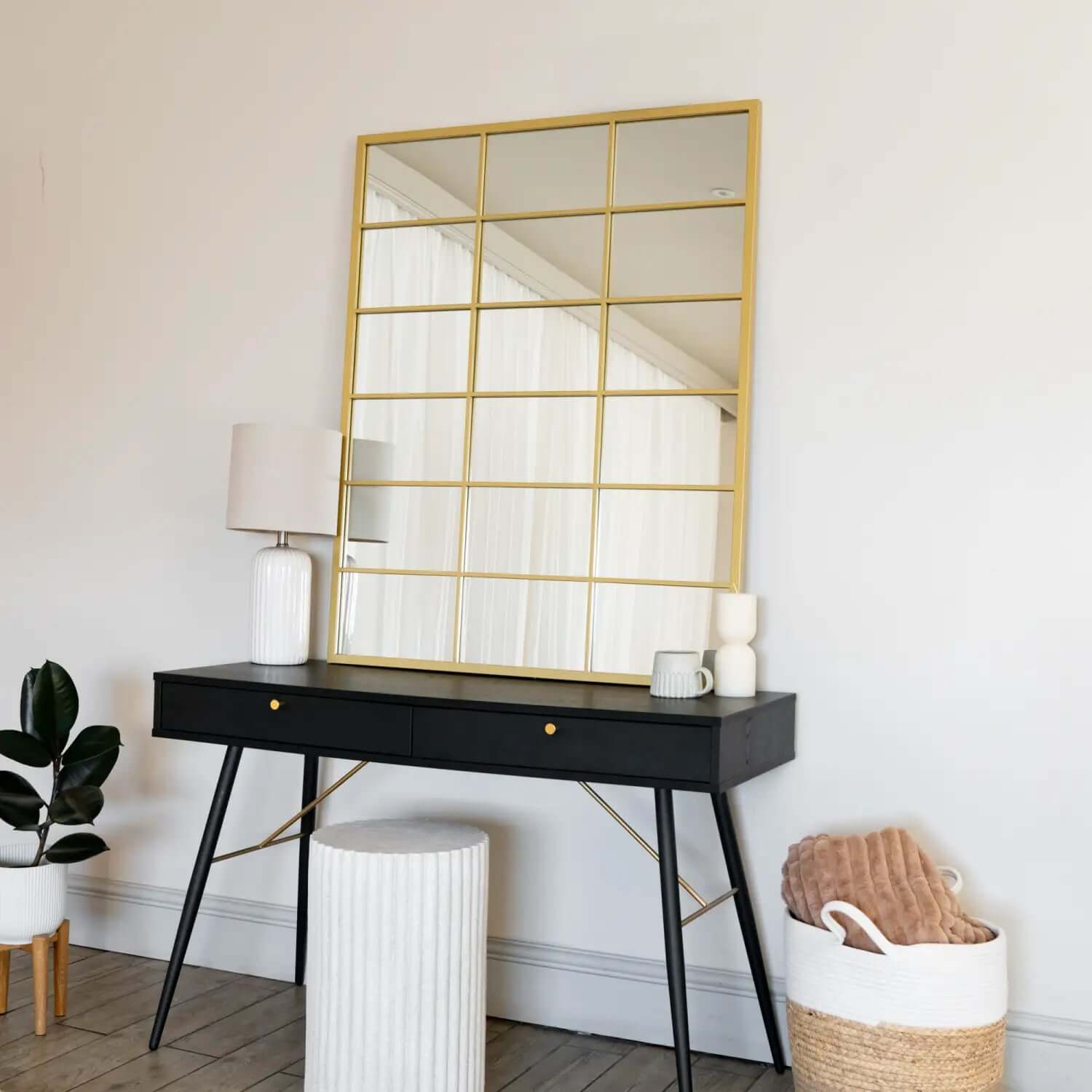 Gold-framed windowpane mirror on a black console table.