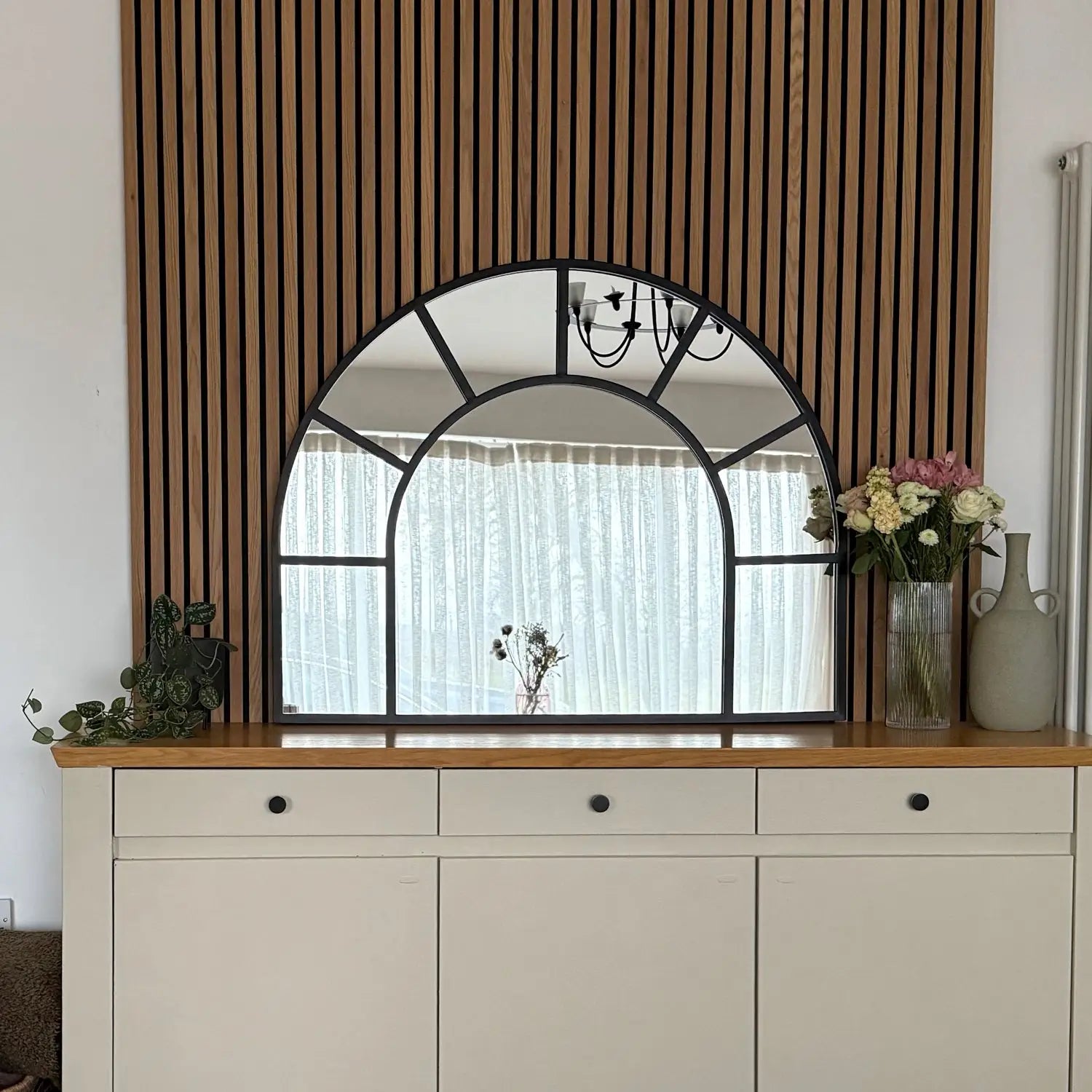 Arched mirror with geometric black frame mounted above a white cabinet.