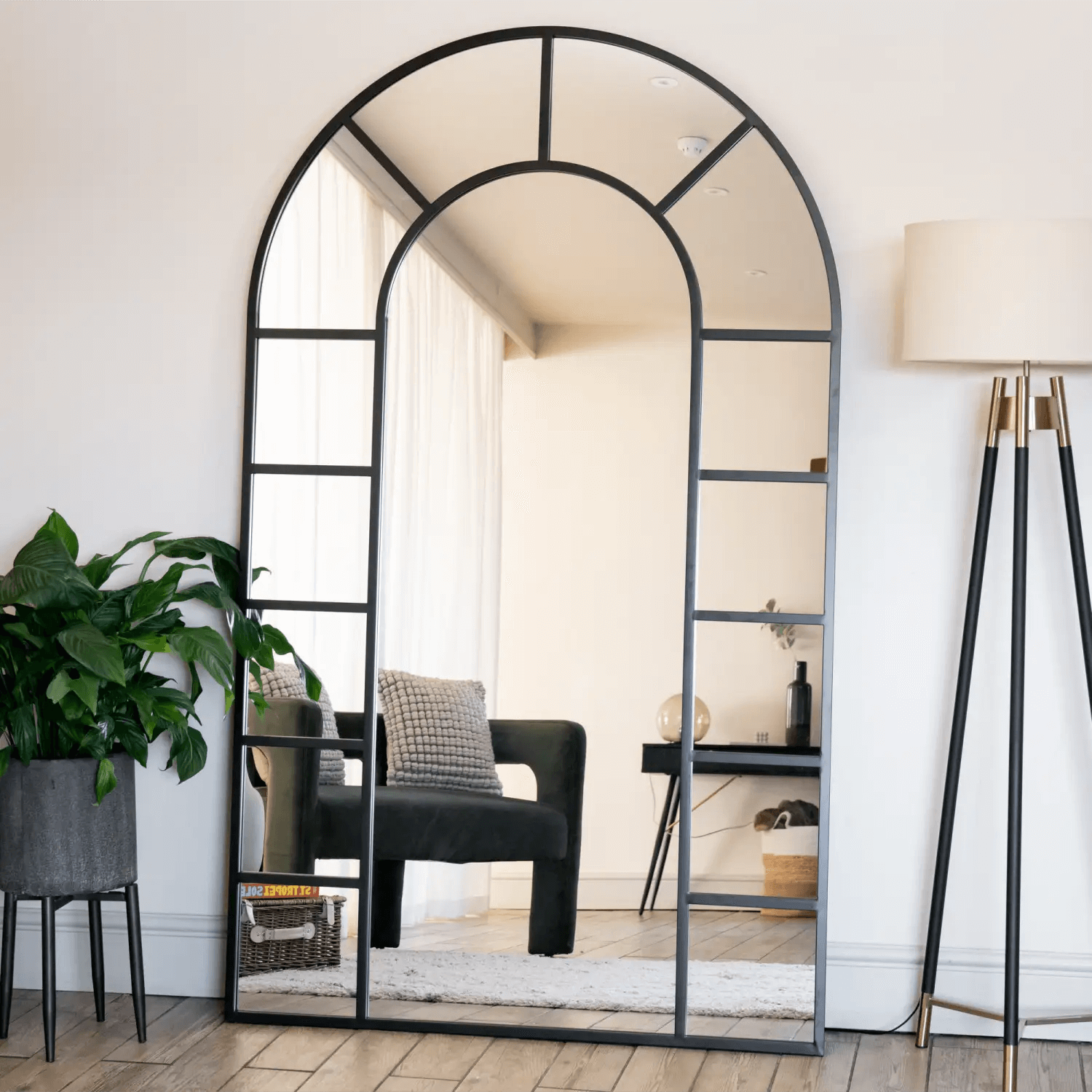 Arched window-style mirror with black metal frame divided into geometric panes.