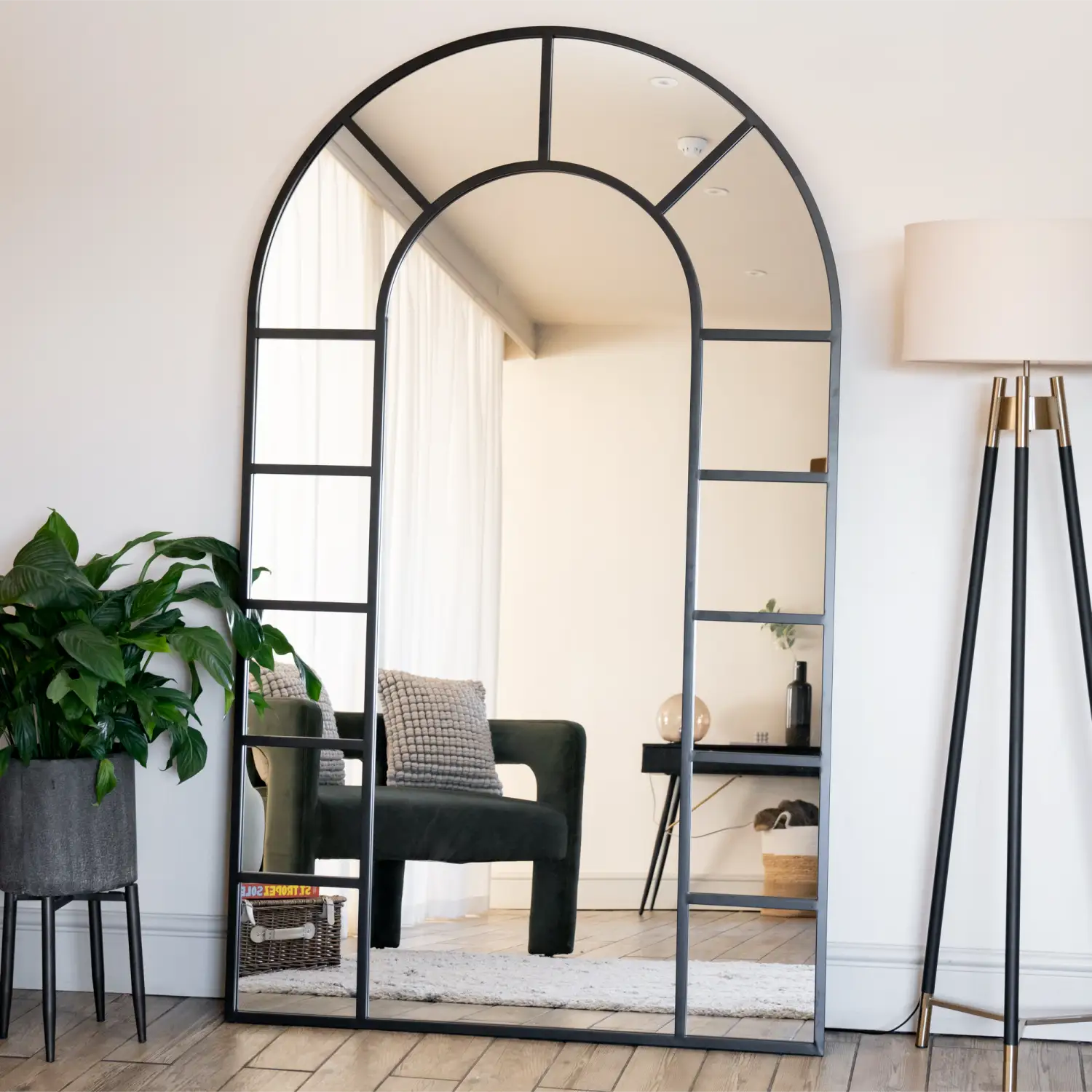 Arched window-style mirror with black metal frame divided into geometric panes.