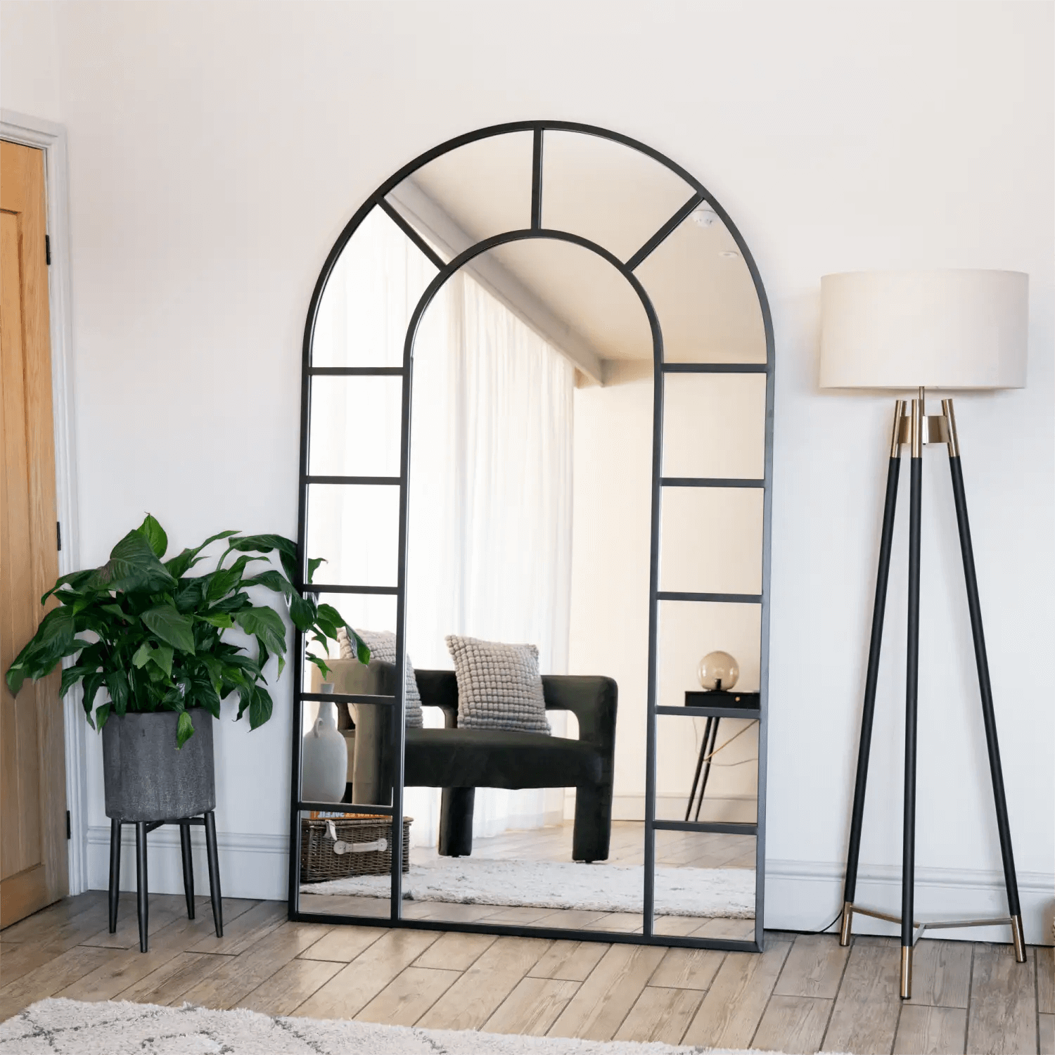 Arched window-style mirror with black metal frame divided into geometric panes.