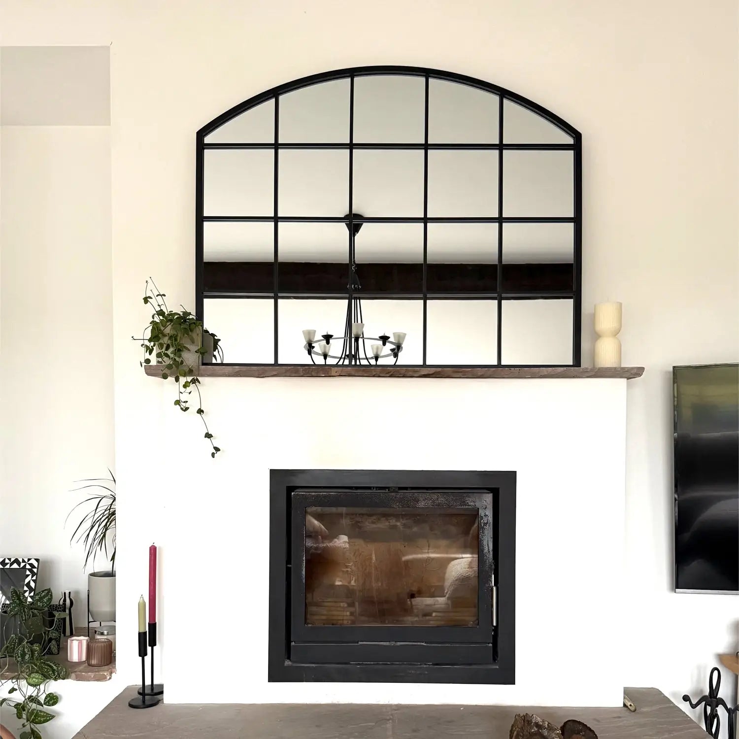 Arched window-style mirror mounted above a black fireplace insert.