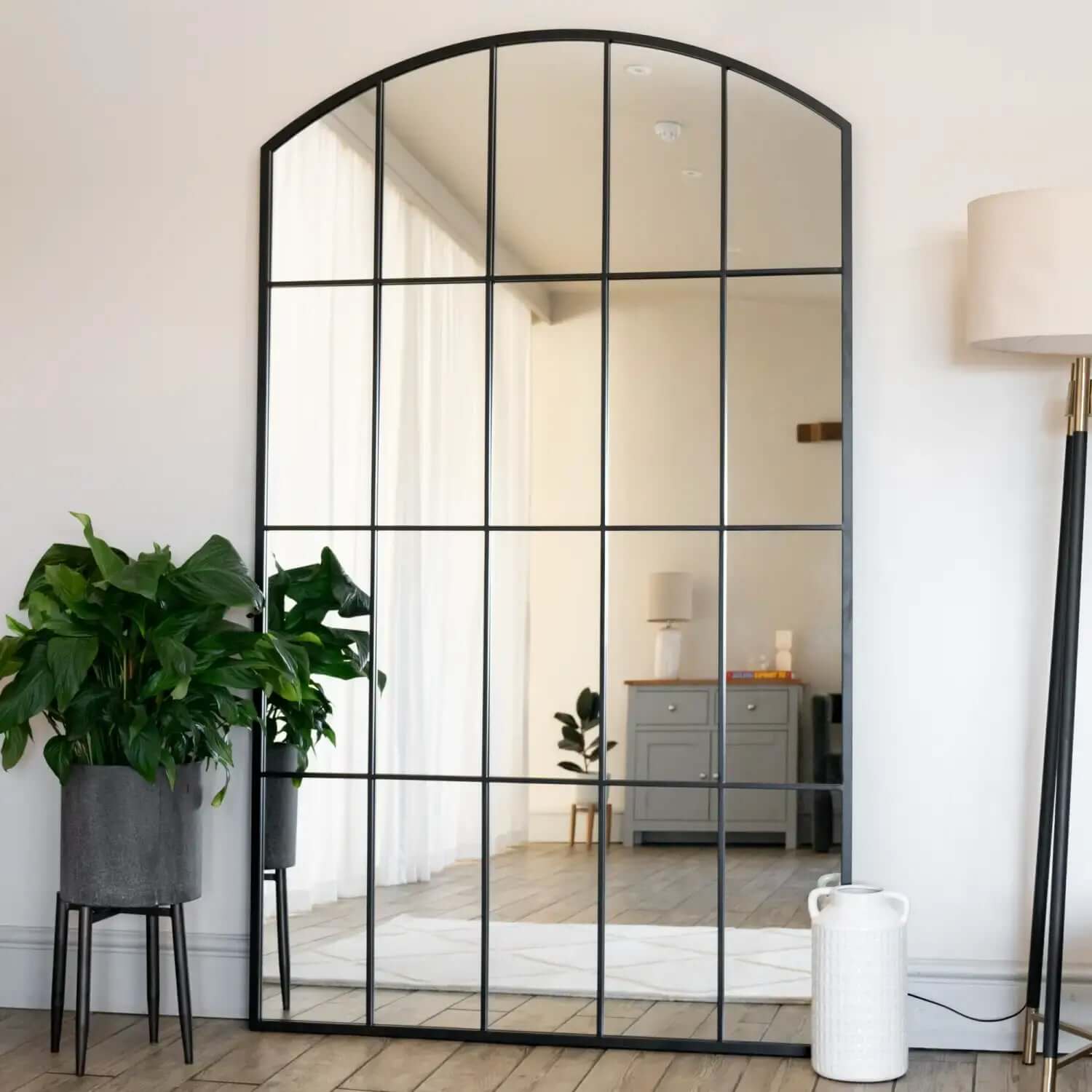 Arched window-style mirror with black metal grid pattern dividing the glass into rectangular sections.