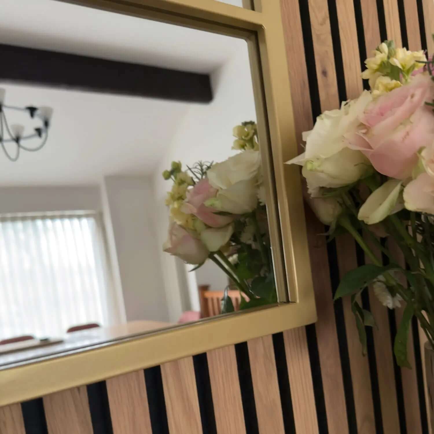 Gold-framed mirror with pink roses reflected in it.