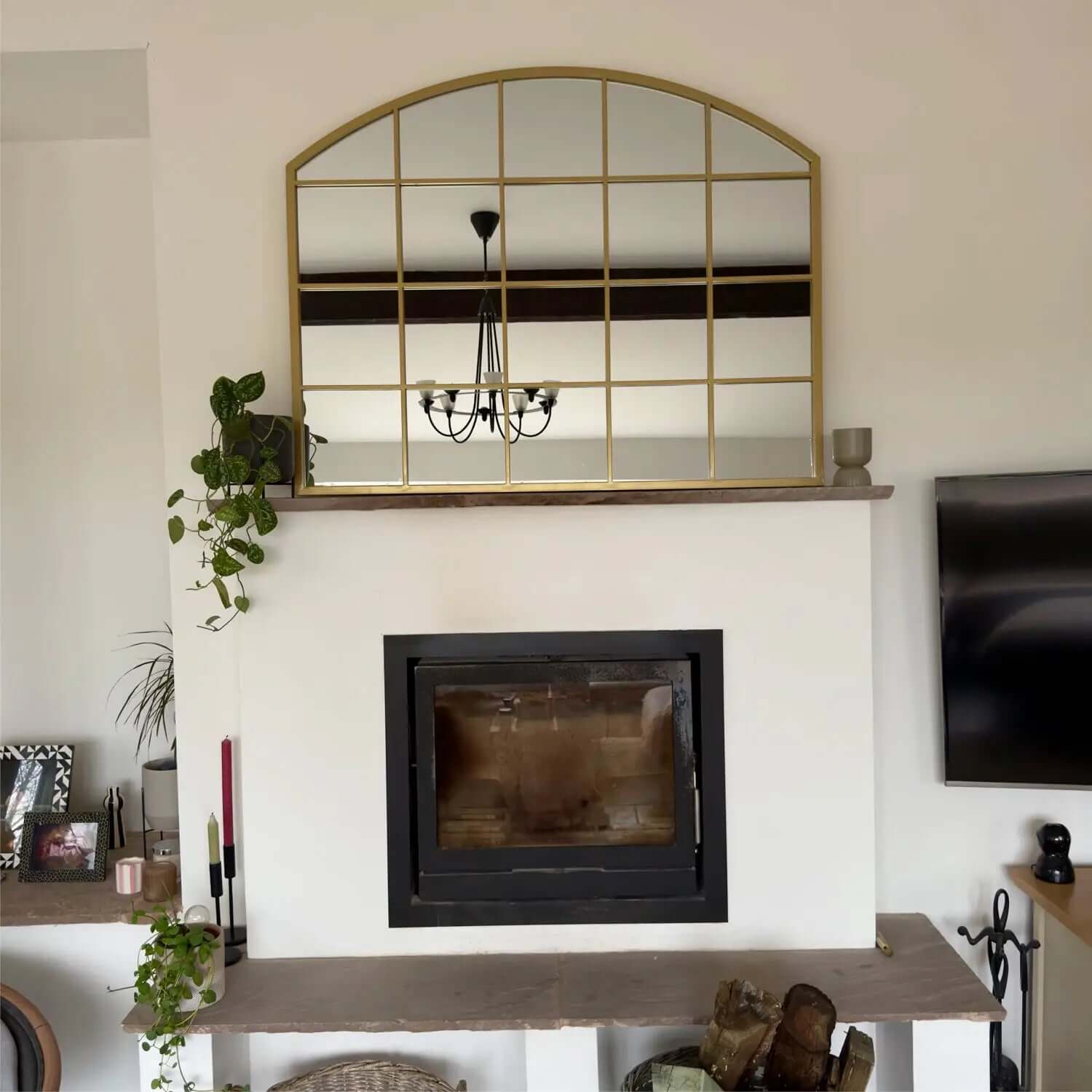 Arched gold-framed mirror mounted above a fireplace.