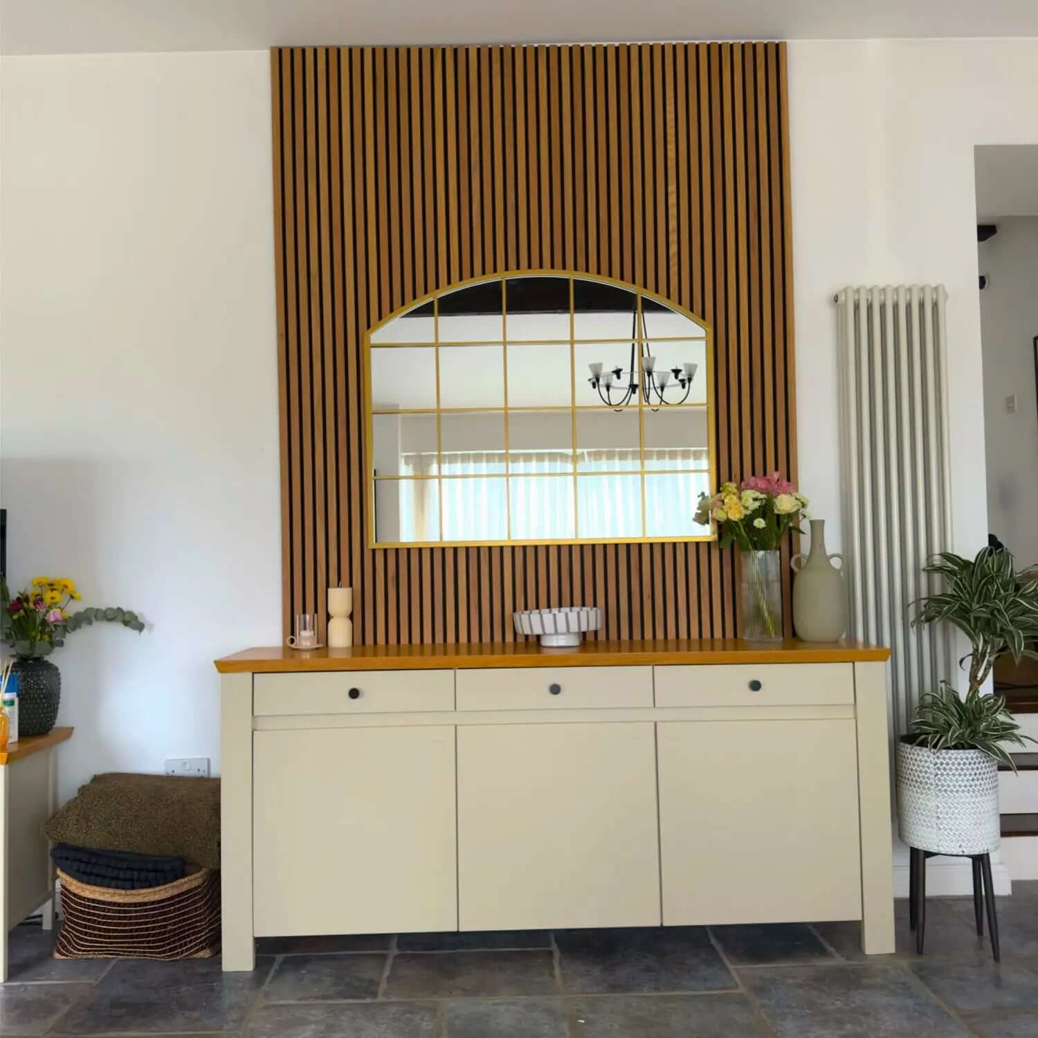 Cream-colored sideboard with wooden top beneath an arched mirror on slatted wood paneling.