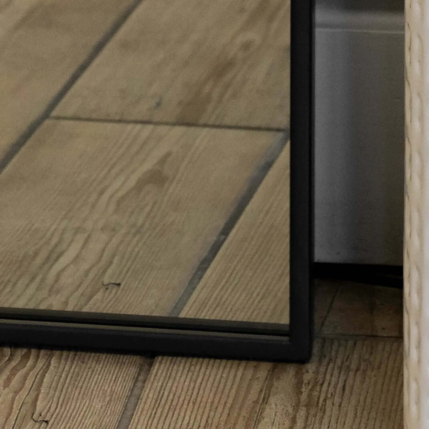 Black-framed mirror resting on wooden flooring.