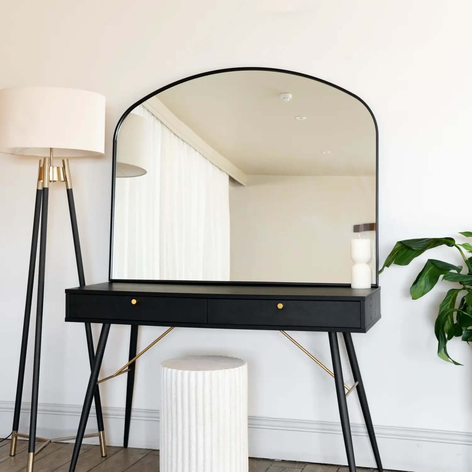 Modern black vanity table with an arched mirror and brass accents.