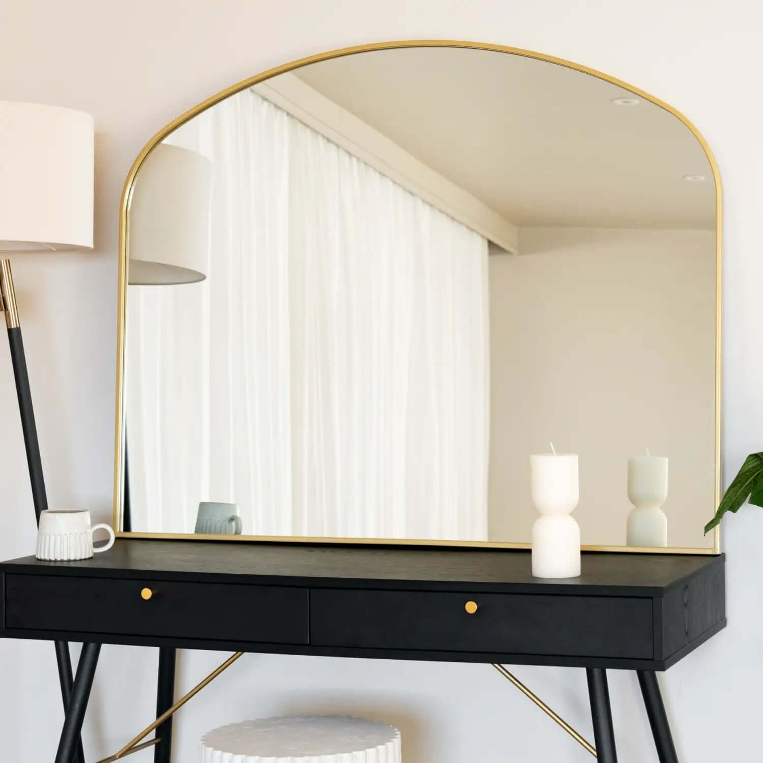 Arched gold-framed mirror mounted above a black console table.