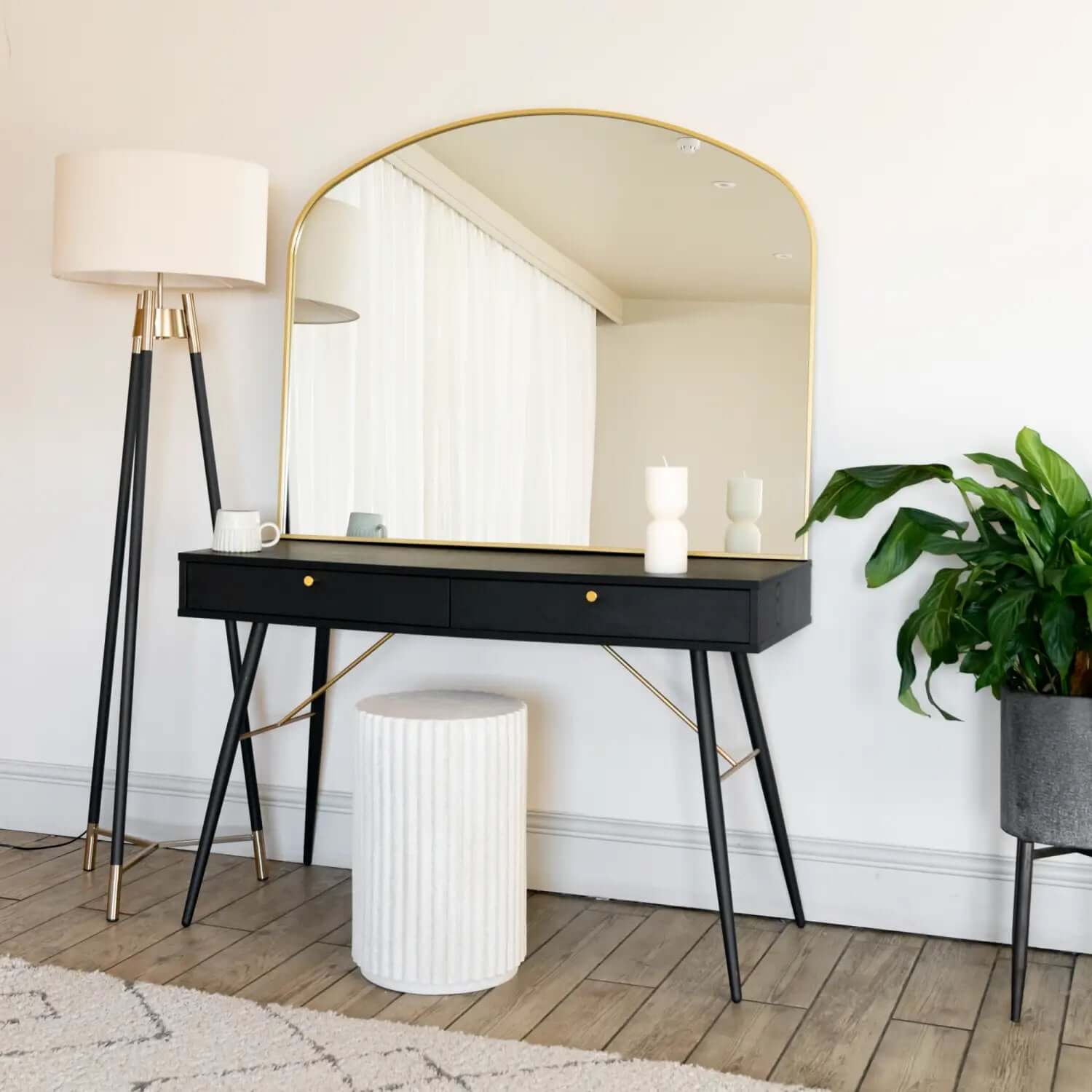 Modern black console table with hairpin legs and a gold-rimmed arched mirror above it.